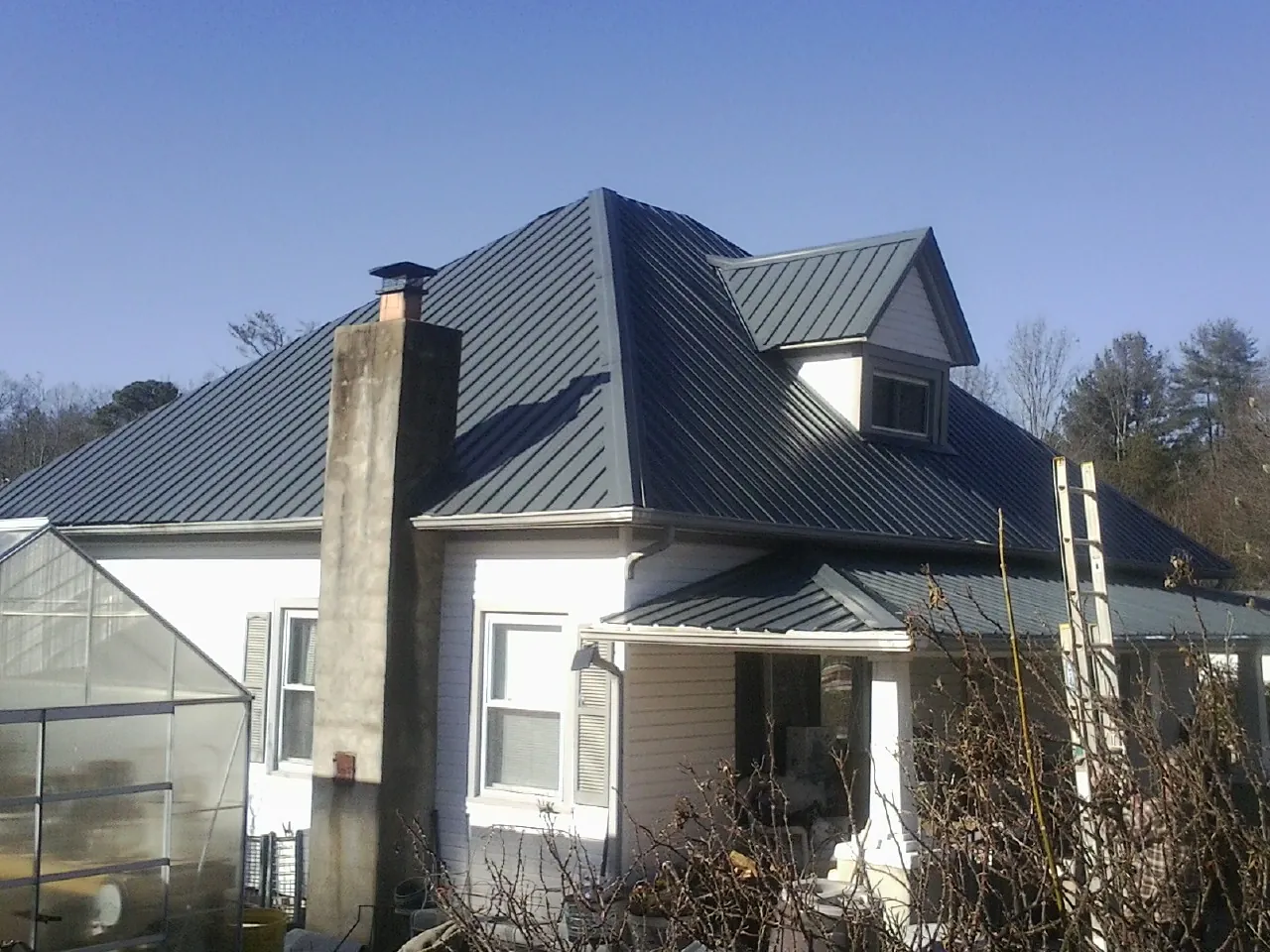 Dark blue standing seam metal roof on a white farmhouse with dormer — Slate & Tile Roof Repair by Roofing Brothers in Arroyo Hondo