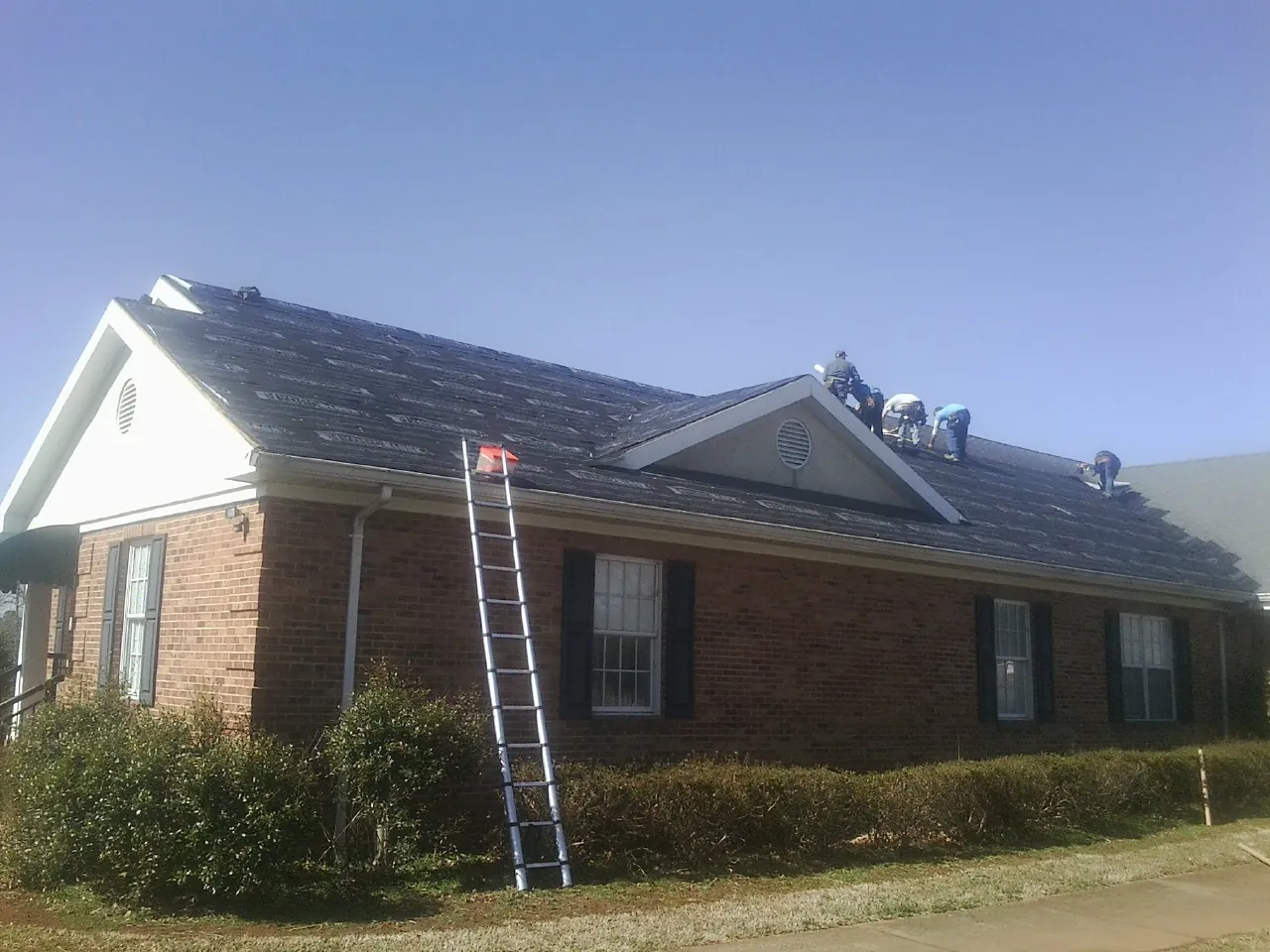 Crew tearing shingles off a brick ranch roof with a ladder set — Metal Roof Repair work by our crew in Arroyo Hondo