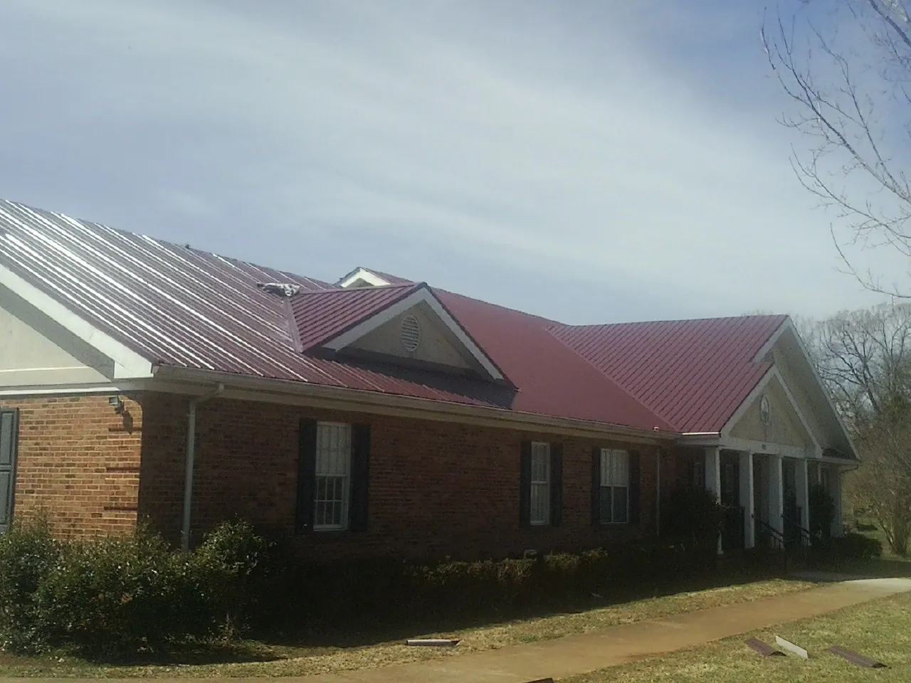 Red metal roof with gabled entries on a long brick building, from a Hail Damage Roof Repair job in Arroyo Hondo