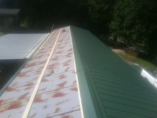 Old rusted panels beside newly installed green metal roofing — Wind Damage Roof Repair by Roofing Brothers in Arroyo Hondo