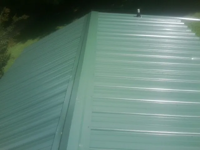 New green metal panels meeting at the ridge of a roof — Flat Roof Repair work by our crew in Arroyo Hondo