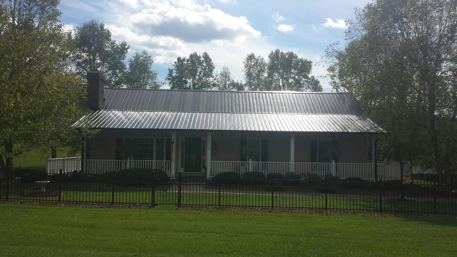 Gray metal roof on a brick ranch with a full width front porch — Gutter Guard Installation work by our crew in Arroyo Hondo