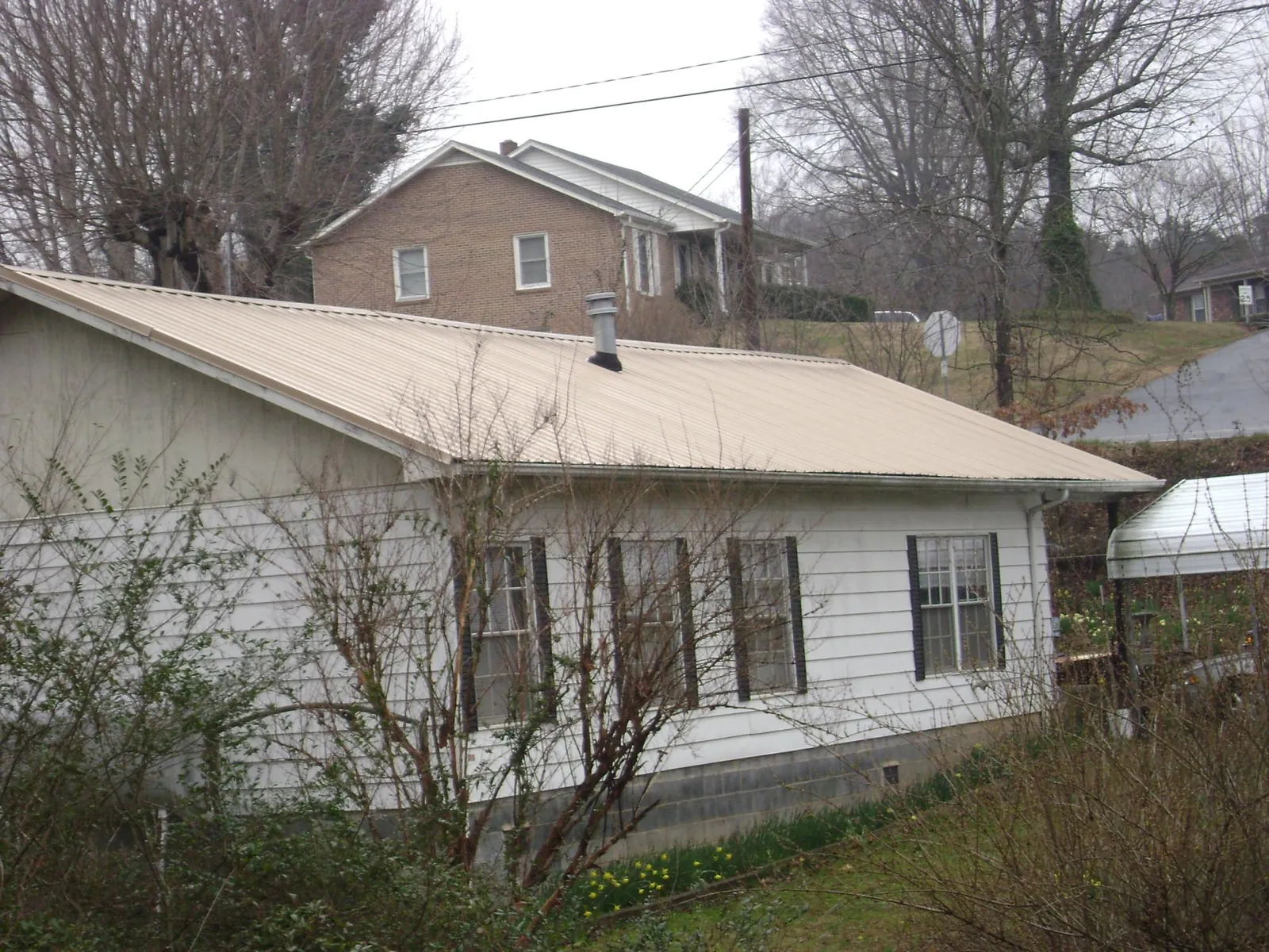Tan metal roof on a white sided house set into a hillside — Commercial Roofing by Roofing Brothers in Arroyo Hondo