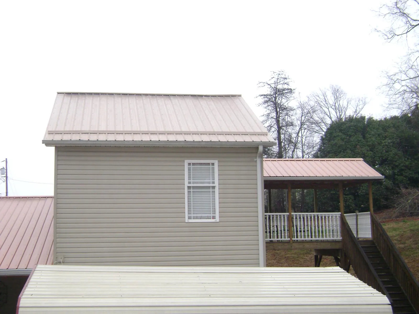 Tan metal roofs on a two story addition and attached porch, from a Roof Replacement job in Arroyo Hondo